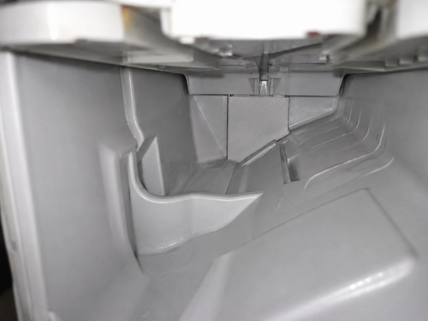 The same dispenser housing cavity after cleaning, bare grey plastic with the siphon channels clear